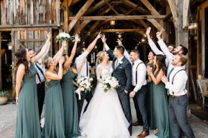 Wedding party celebrating with bride and groom outside rustic barn venue.